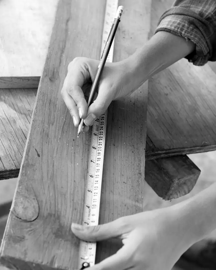 Mains qui tracent un trait de crayon le long d’un mètre ruban posé sur une planche