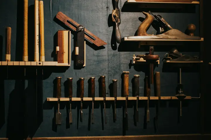 Rabots, ciseaux à bois et outils accrochés sur le mur sombre d’un atelier.