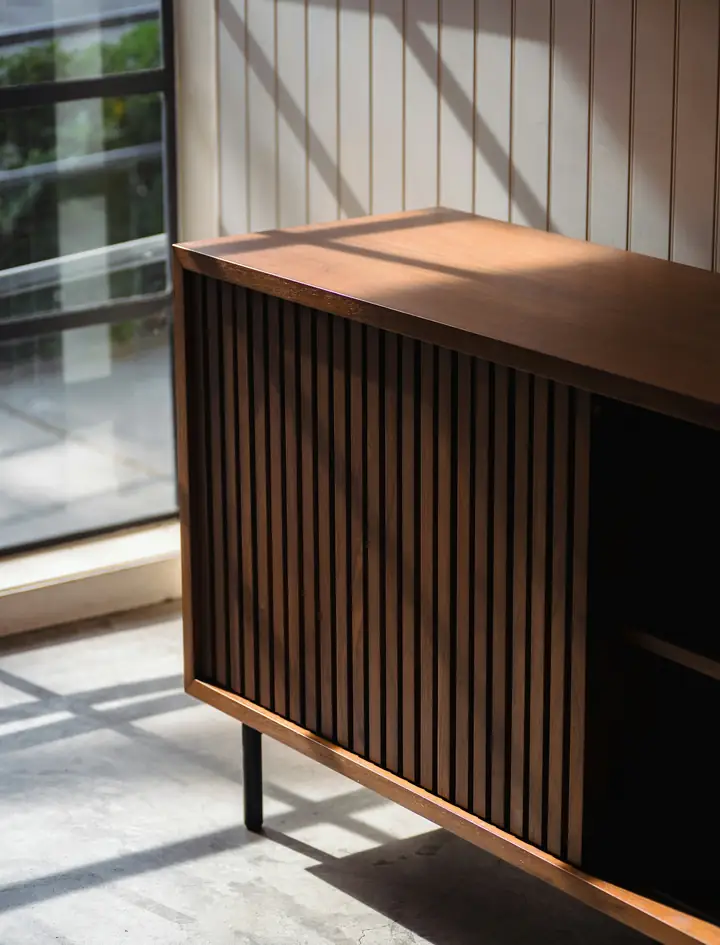 Intérieur de l’armoire : un buffet en noyer massif, à lamelles verticales, dans une lumière chaude.